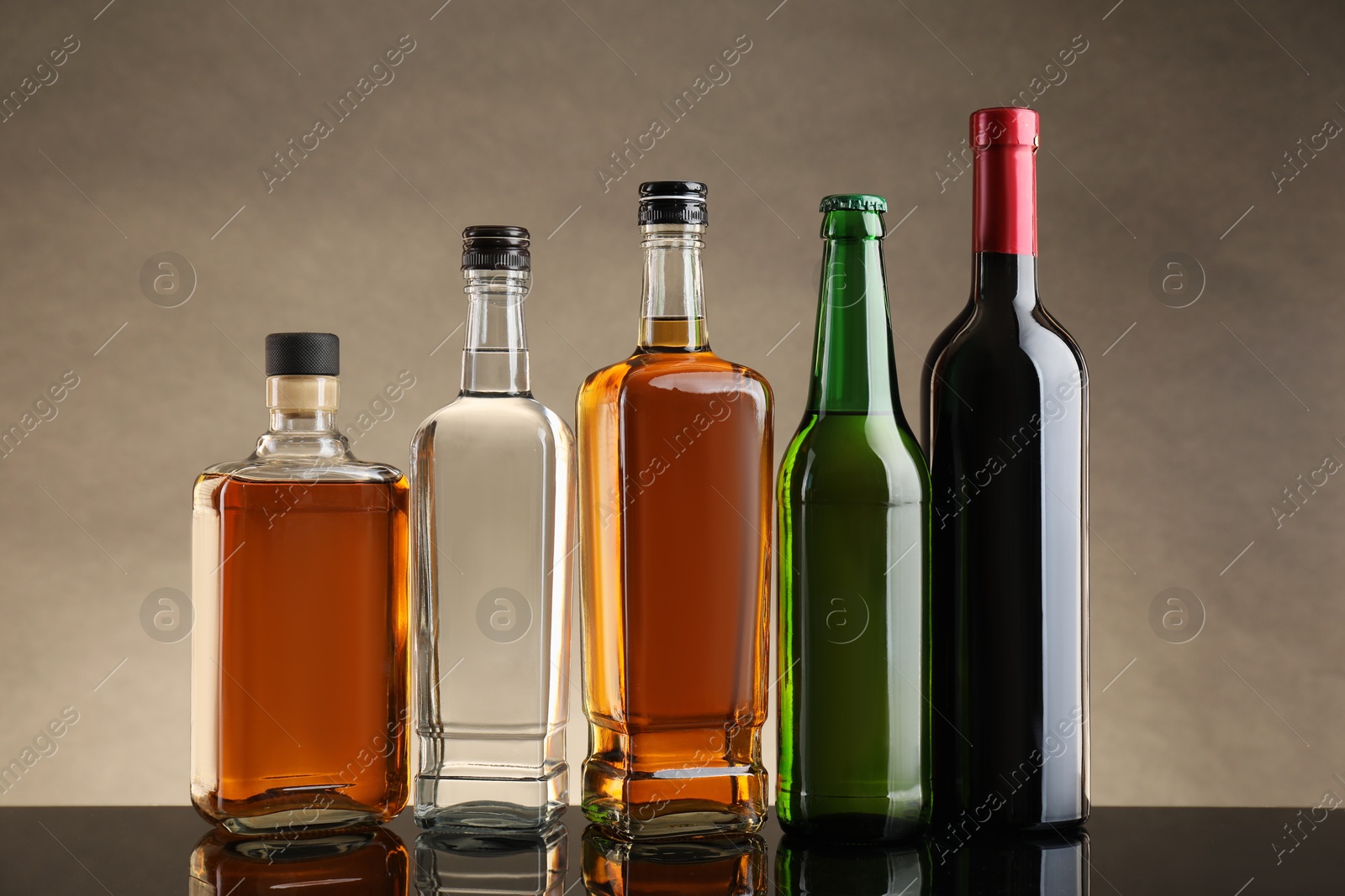 Photo of Bottles with different alcoholic drinks on table against beige background