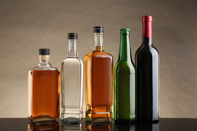 Bottles with different alcoholic drinks on table against beige background