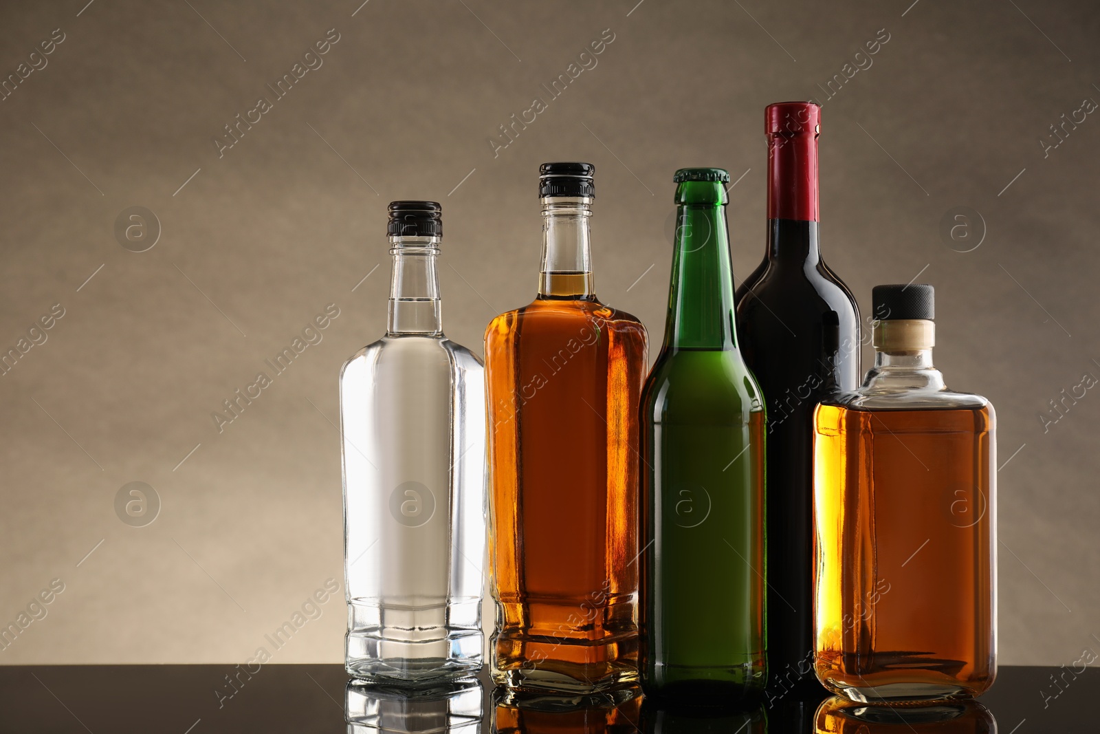 Photo of Bottles with different alcoholic drinks on table against beige background. Space for text