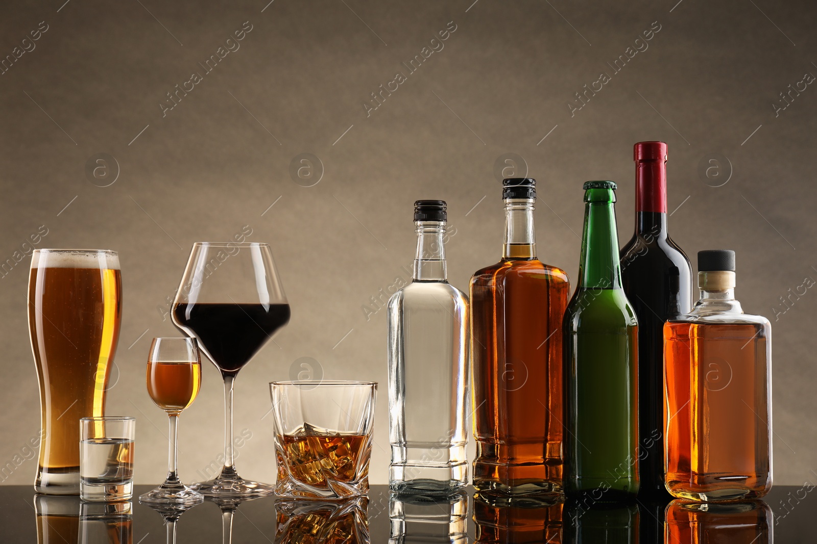 Photo of Bottles and glasses with different alcoholic drinks on table against beige background