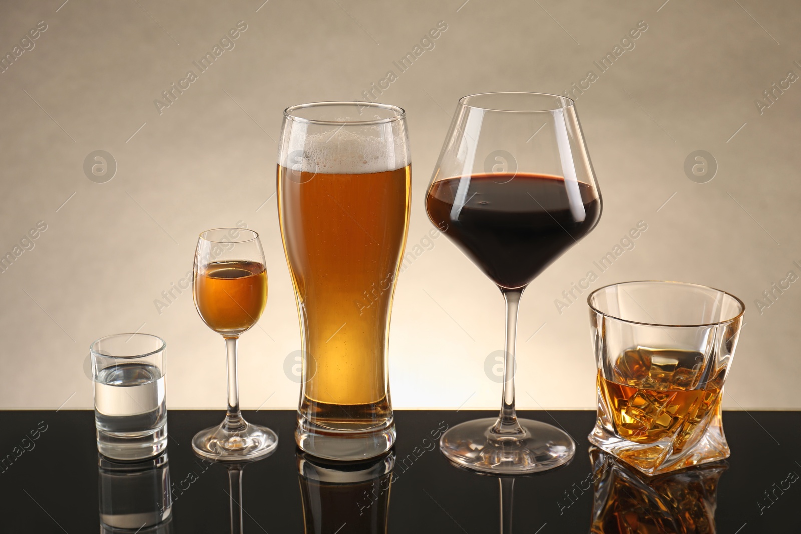 Photo of Glasses with different alcoholic drinks on table against beige background