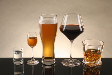 Glasses with different alcoholic drinks on table against beige background