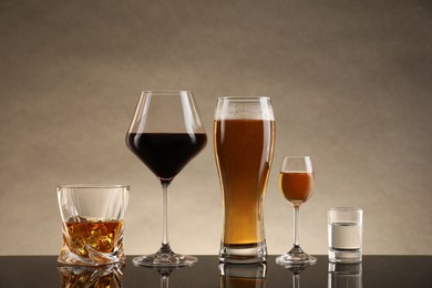 Glasses with different alcoholic drinks on table against beige background