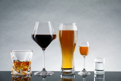 Glasses with different alcoholic drinks on table against light gray background