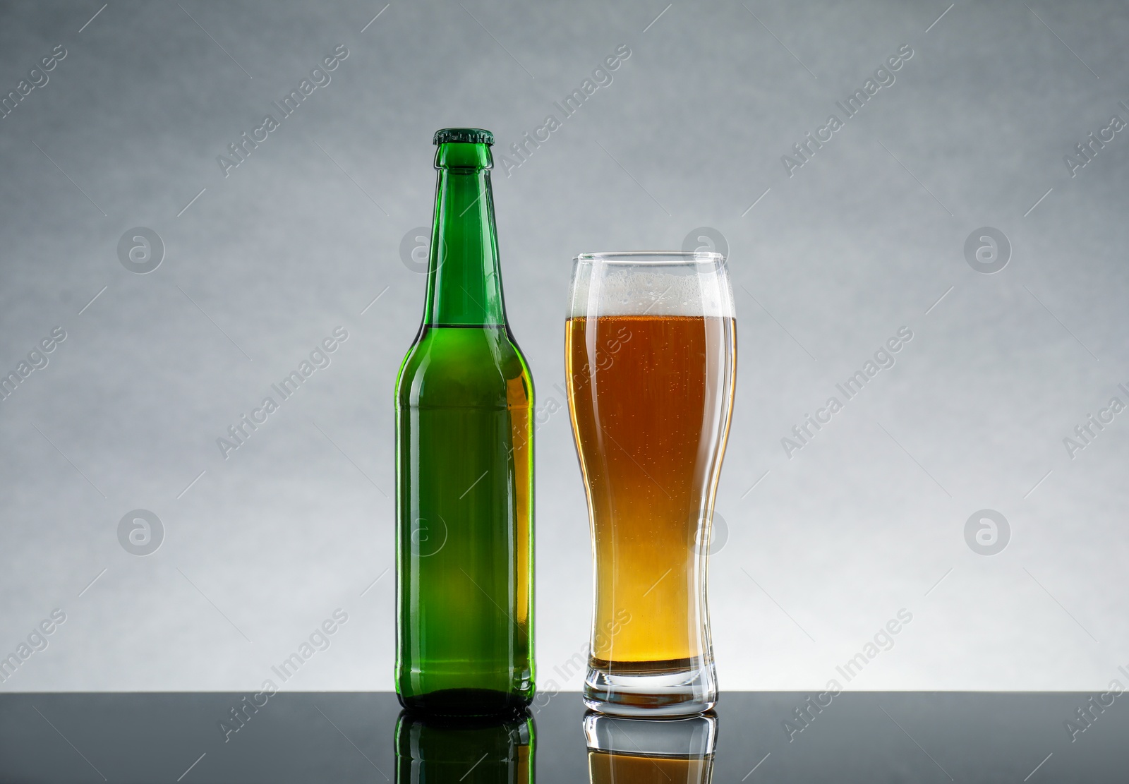 Photo of Bottle and glass of beer on table against light gray background