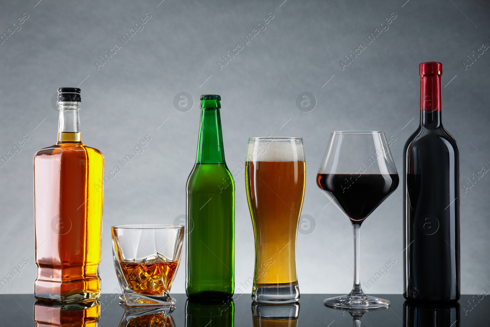 Photo of Bottles and glasses with different alcoholic drinks on table against light gray background