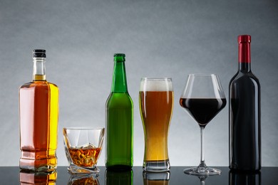 Photo of Bottles and glasses with different alcoholic drinks on table against light gray background