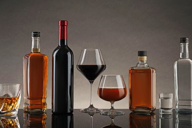 Photo of Bottles and glasses with different alcoholic drinks on table against gray background