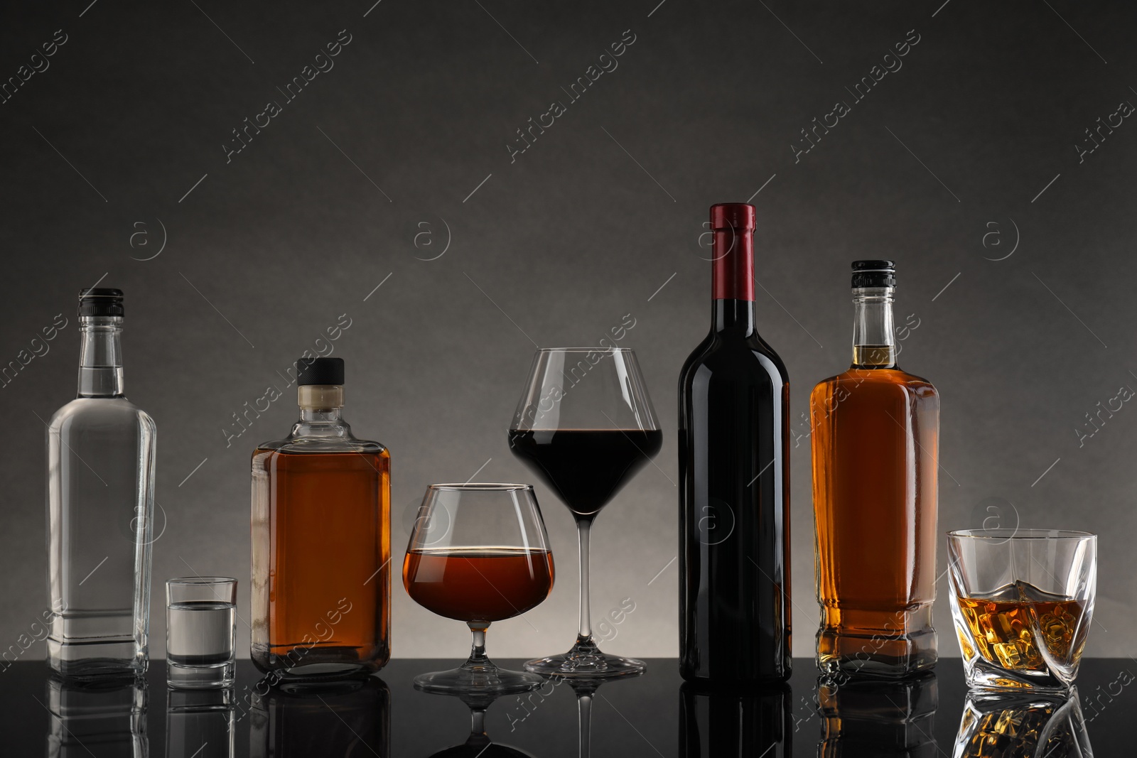 Photo of Bottles and glasses with different alcoholic drinks on table against gray background