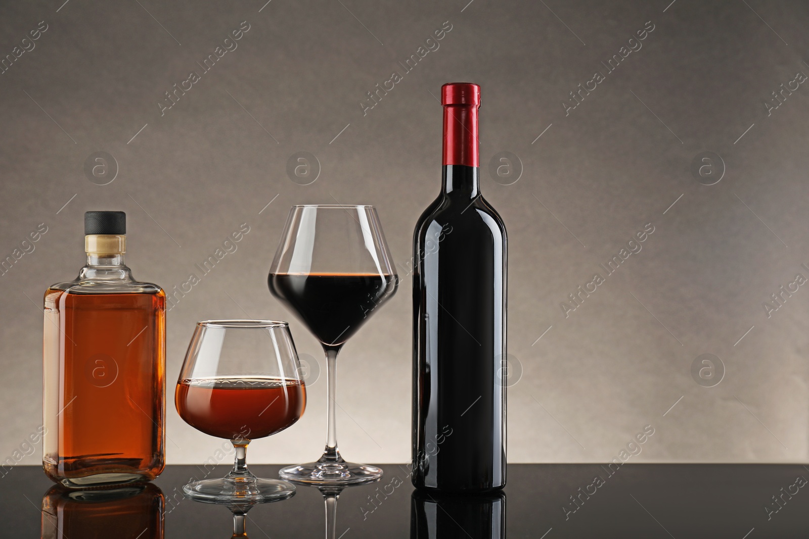 Photo of Bottles and glasses with different alcoholic drinks on table against gray background, space for text