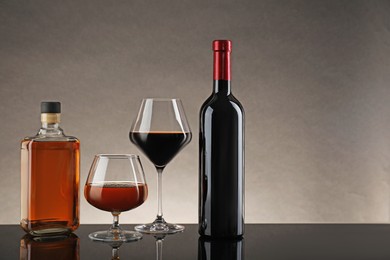 Bottles and glasses with different alcoholic drinks on table against gray background, space for text