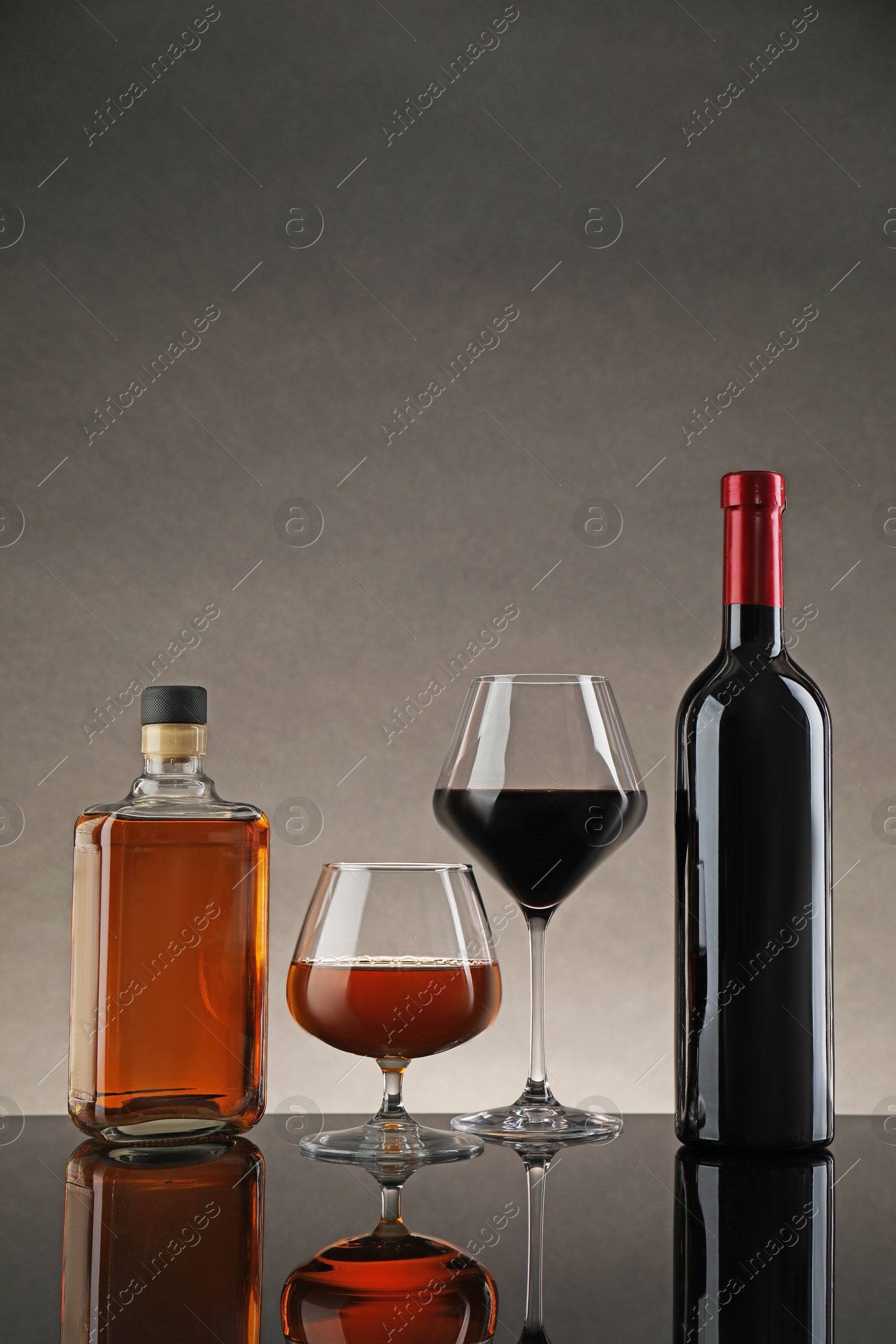 Photo of Bottles and glasses with different alcoholic drinks on table against gray background