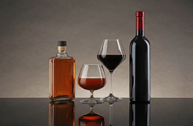 Photo of Bottles and glasses with different alcoholic drinks on table against gray background