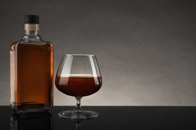 Photo of Bottle and glass with whiskey on table against gray background, space for text