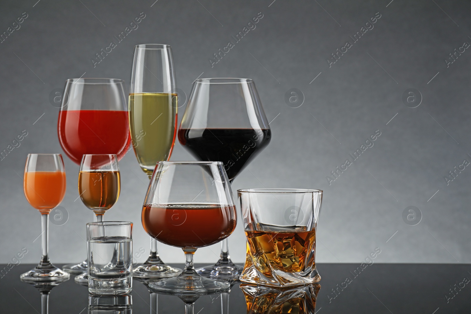 Photo of Glasses with different alcoholic drinks on table against gray background, space for text