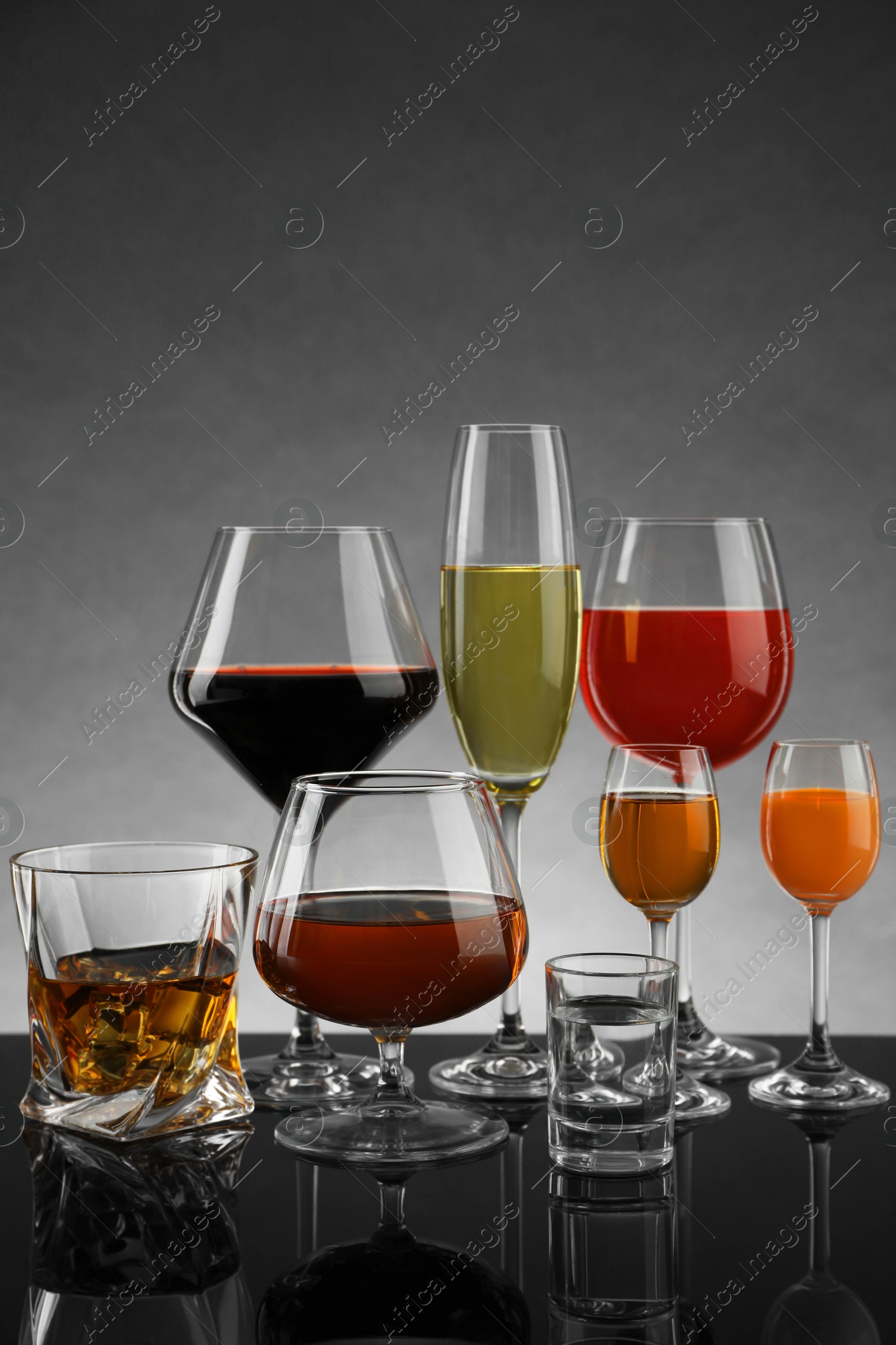 Photo of Glasses with different alcoholic drinks on table against gray background