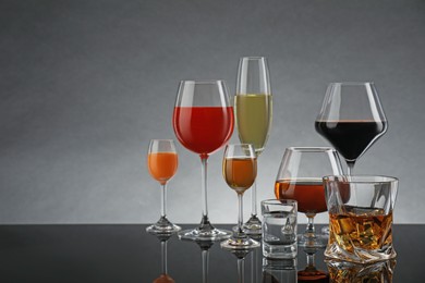 Glasses with different alcoholic drinks on table against gray background, space for text