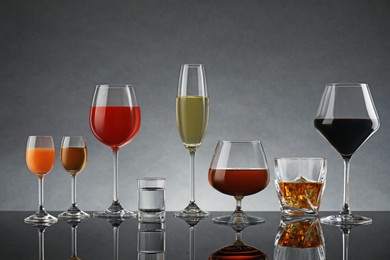 Glasses with different alcoholic drinks on table against gray background