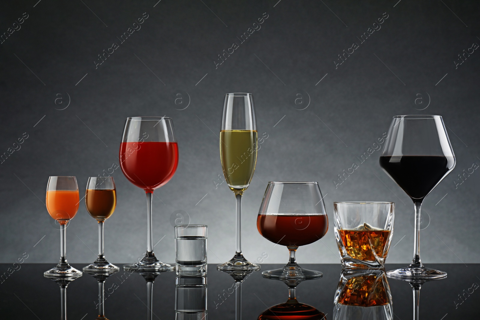 Photo of Glasses with different alcoholic drinks on table against gray background