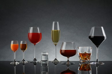 Glasses with different alcoholic drinks on table against gray background