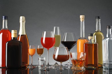 Photo of Bottles and glasses with different alcoholic drinks on table against gray background