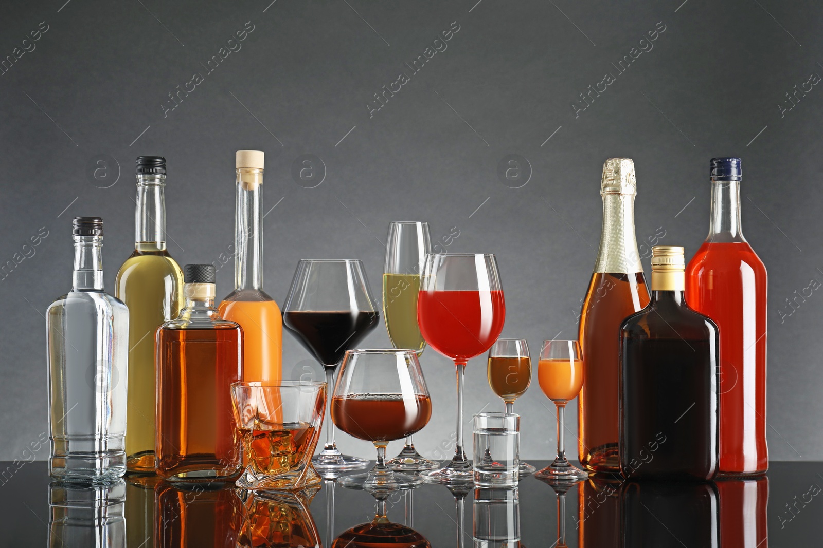 Photo of Bottles and glasses with different alcoholic drinks on table against gray background