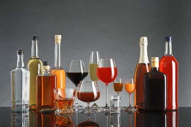 Bottles and glasses with different alcoholic drinks on table against gray background