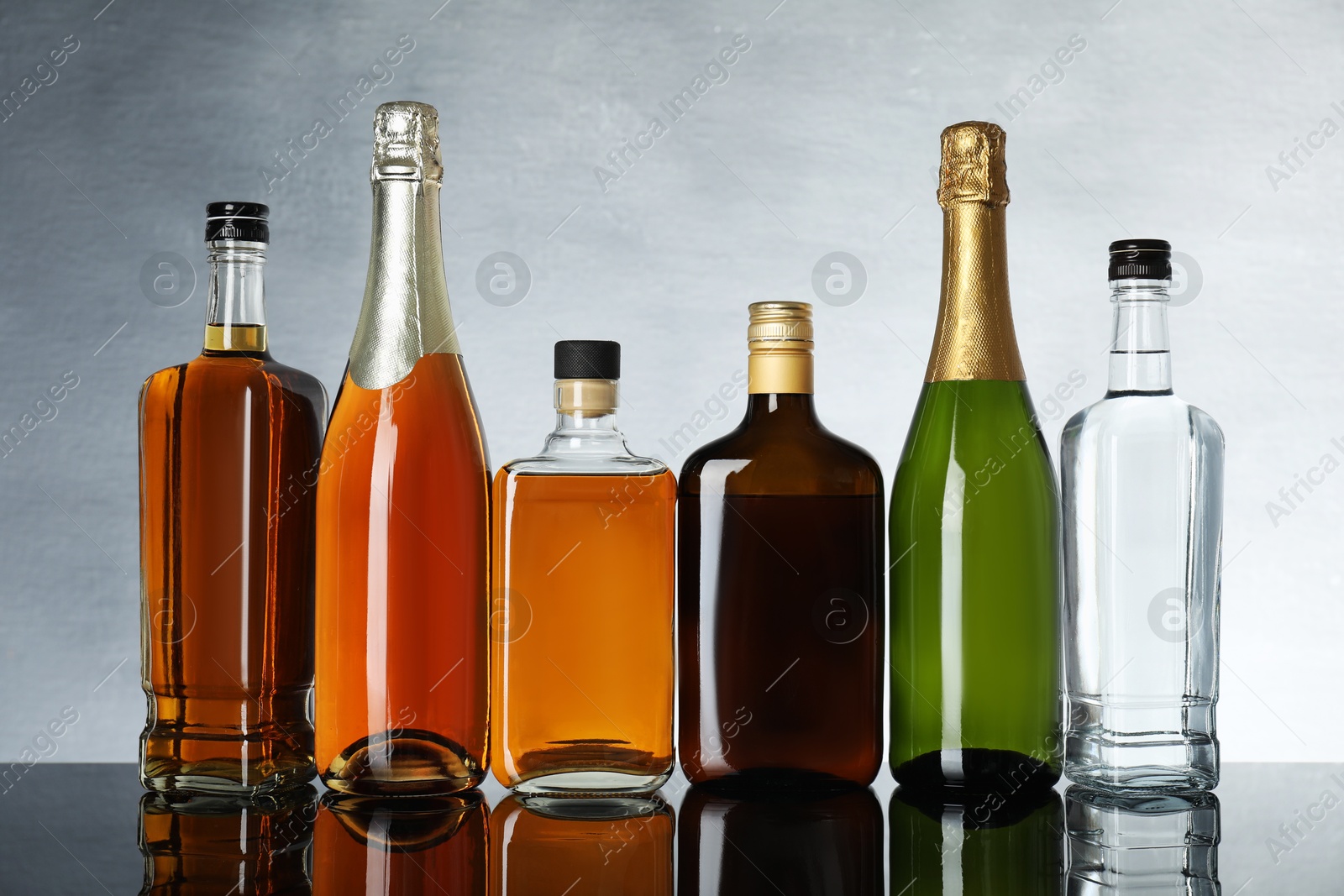 Photo of Bottles of different alcoholic drinks on table against light gray background