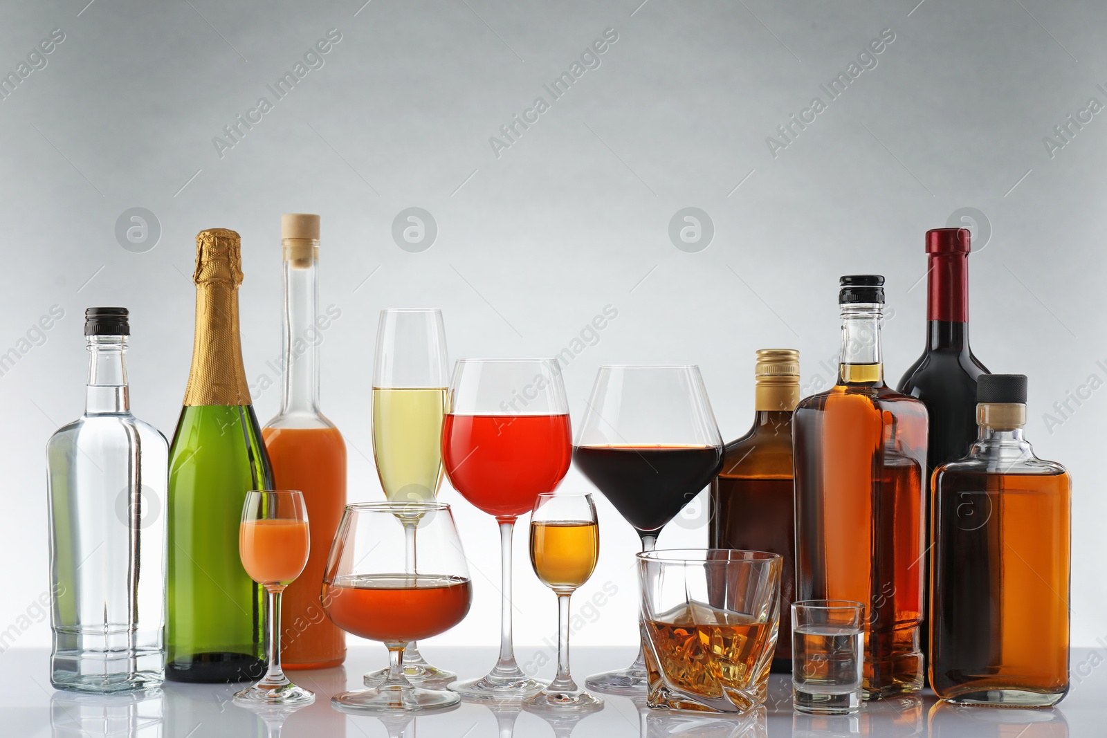 Photo of Bottles and glasses with different alcoholic drinks on white table against light background