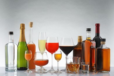 Bottles and glasses with different alcoholic drinks on white table against light background