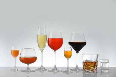 Photo of Glasses with different alcoholic drinks on white table against light background