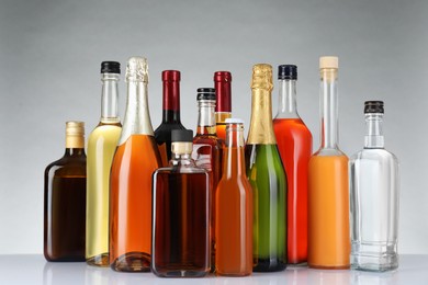 Photo of Bottles of different alcoholic drinks on white table against light background