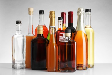 Photo of Bottles of different alcoholic drinks on white table against light background