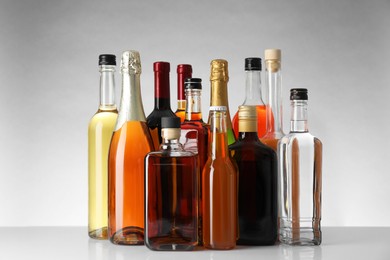 Photo of Bottles of different alcoholic drinks on white table against light background