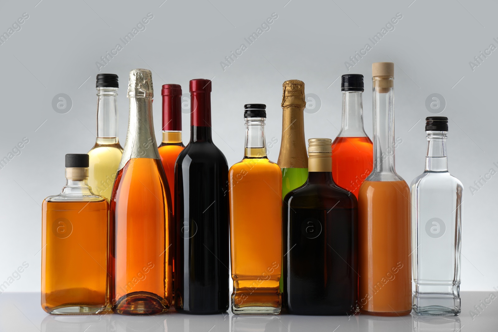 Photo of Bottles of different alcoholic drinks on white table against light background