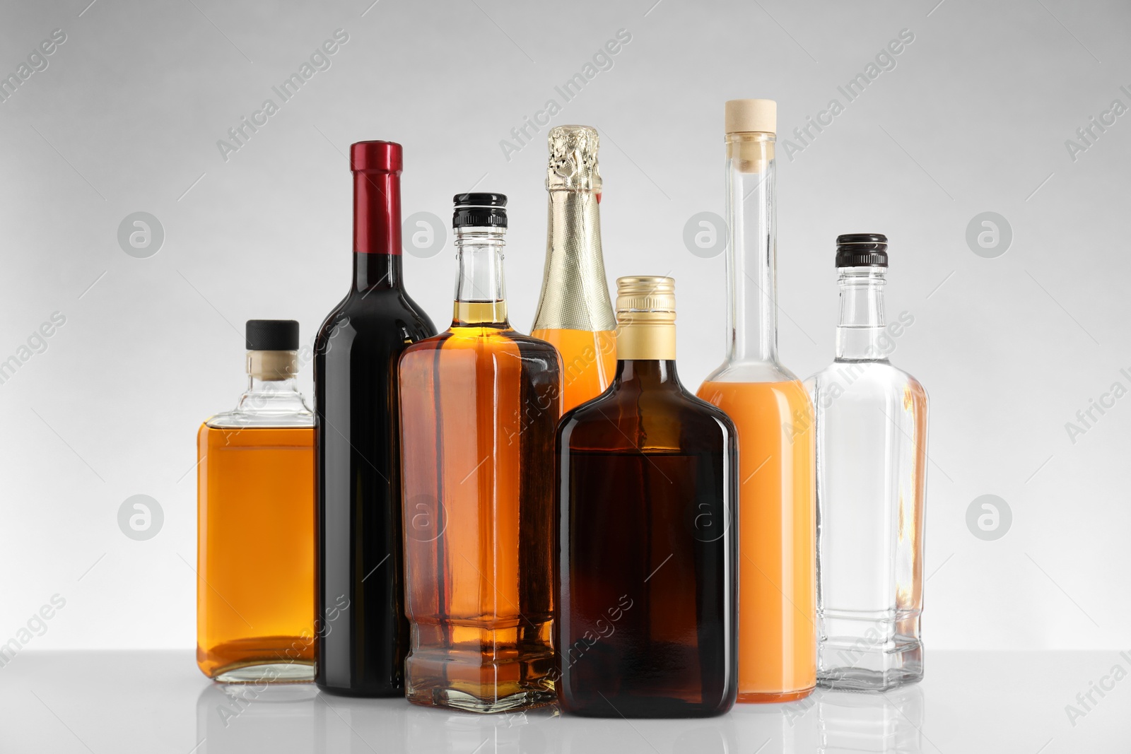 Photo of Bottles of different alcoholic drinks on white table against light background