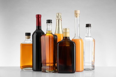 Photo of Bottles of different alcoholic drinks on white table against light background