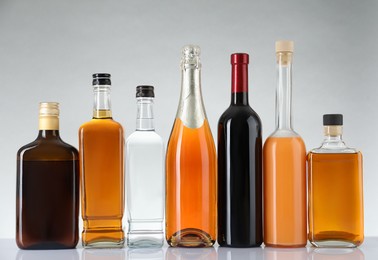 Photo of Bottles of different alcoholic drinks on white table against light background