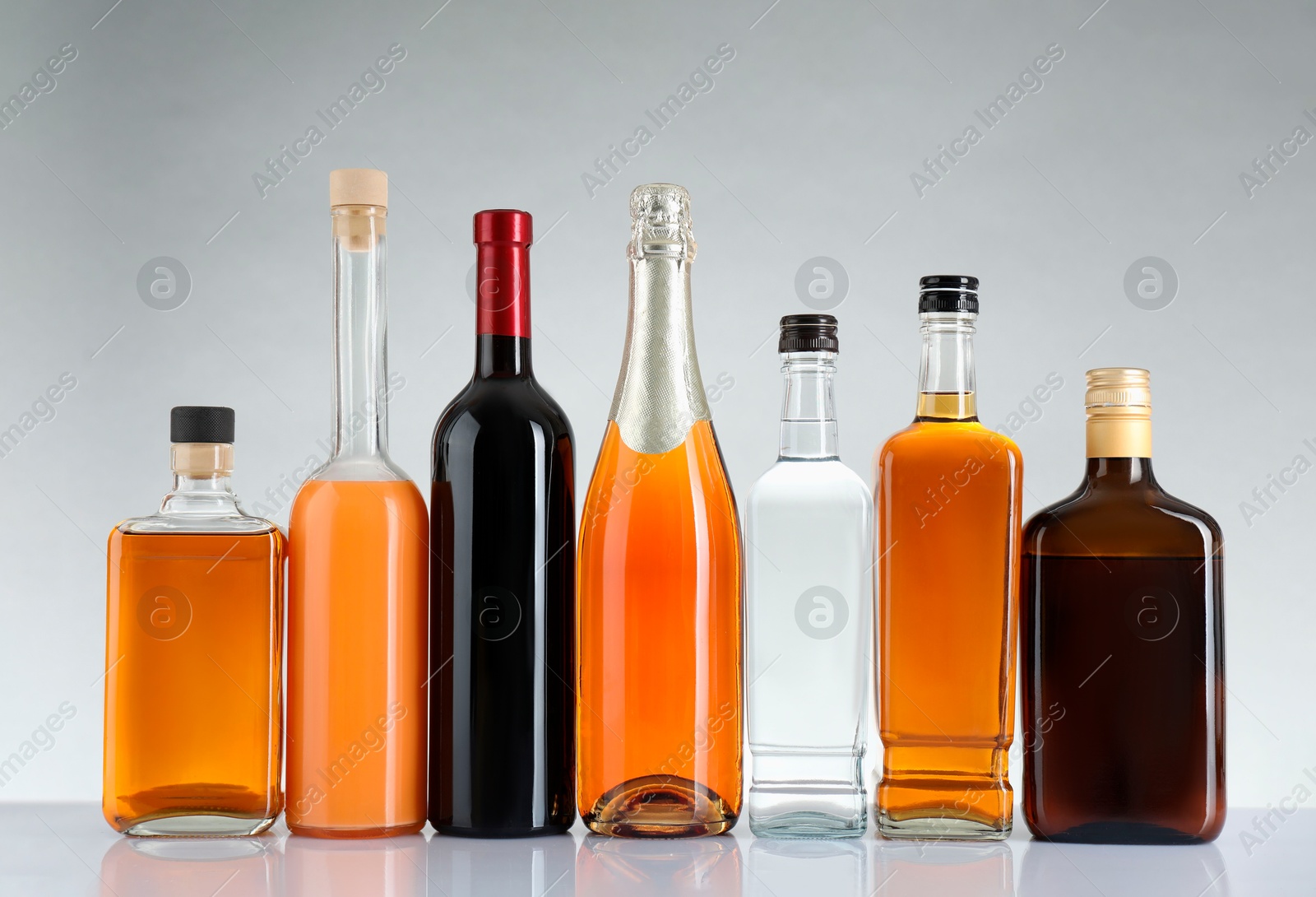 Photo of Bottles of different alcoholic drinks on white table against light background