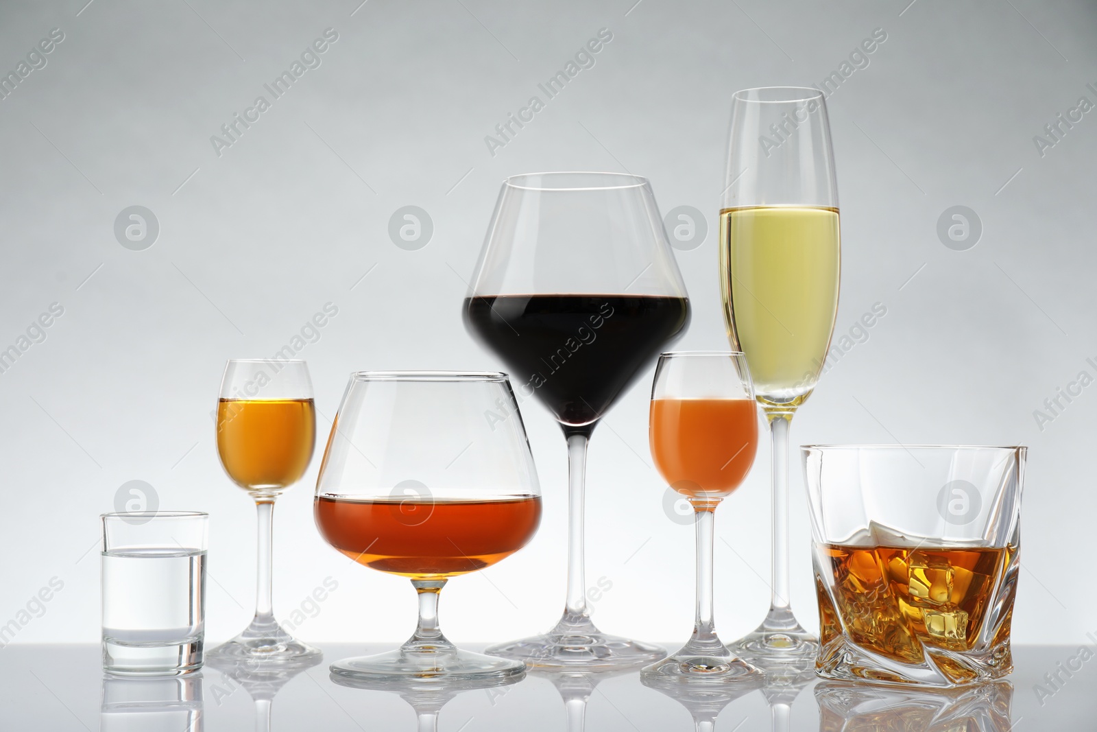 Photo of Glasses with different alcoholic drinks on white table against light background