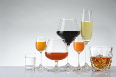 Glasses with different alcoholic drinks on white table against light background