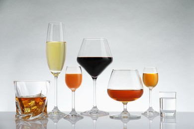 Photo of Glasses with different alcoholic drinks on white table against light background