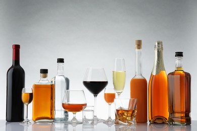 Bottles and glasses with different alcoholic drinks on white table against light background