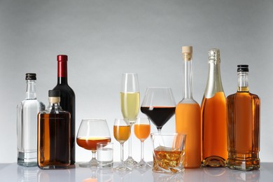 Photo of Bottles and glasses with different alcoholic drinks on white table against light background