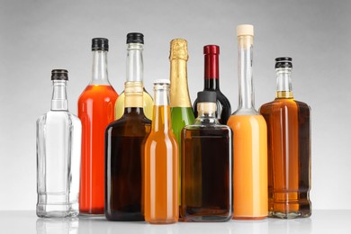 Photo of Bottles of different alcoholic drinks on white table against light background