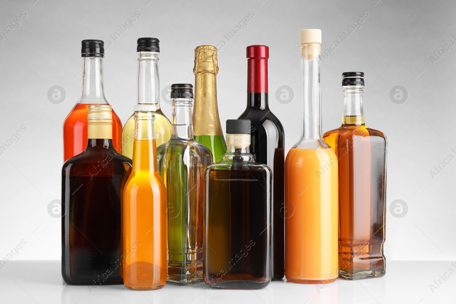 Photo of Bottles of different alcoholic drinks on white table against light background