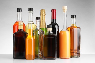 Bottles of different alcoholic drinks on white table against light background