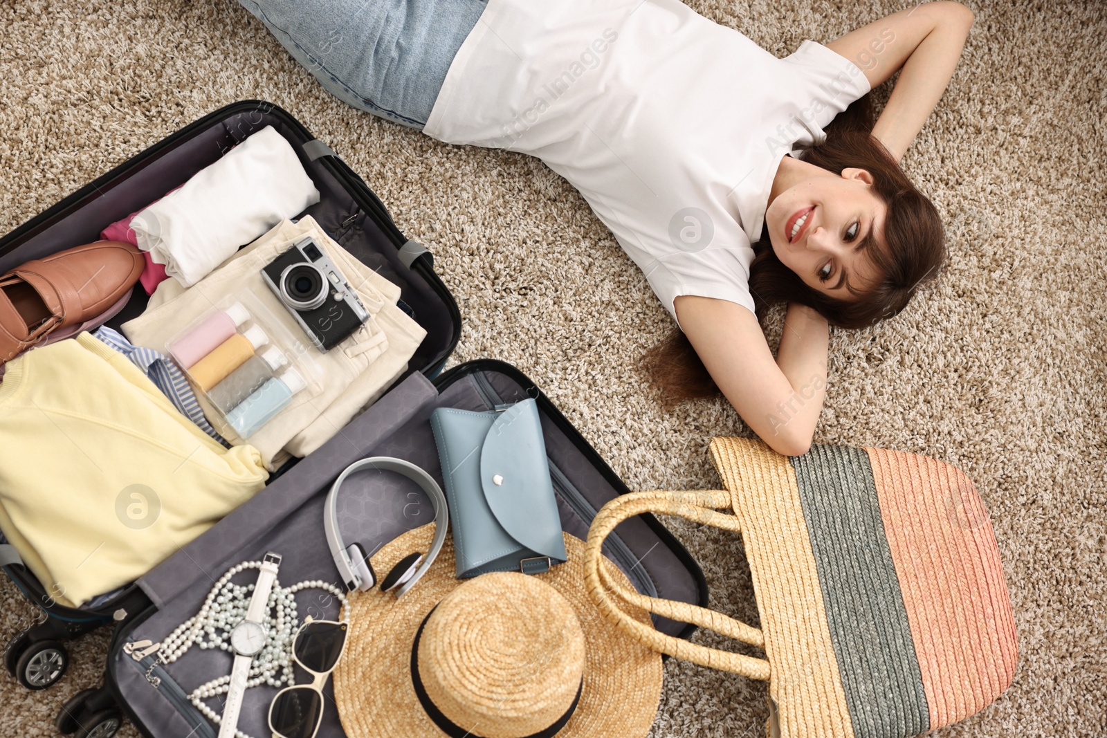 Photo of Woman packing suitcase for trip on floor indoors, top view