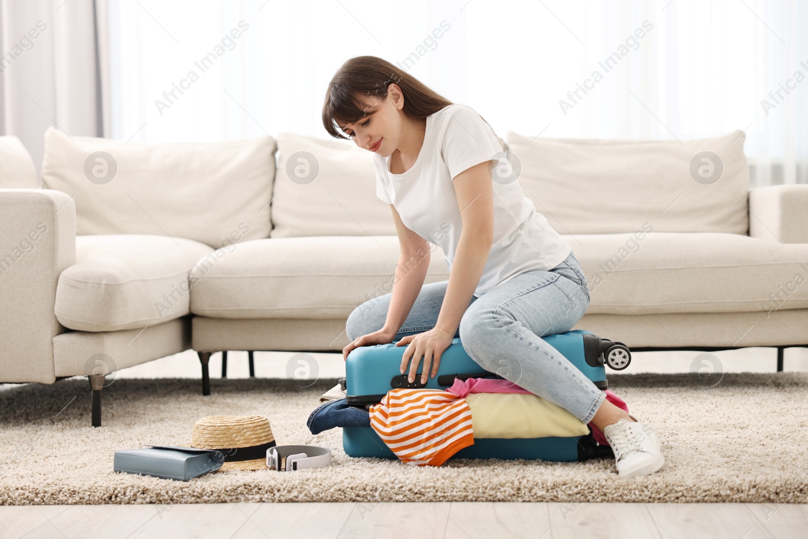 Photo of Woman packing suitcase for trip on floor indoors