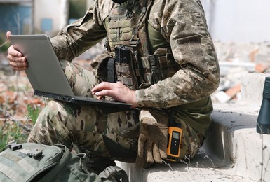 Military mission. Soldier in uniform using laptop near abandoned building outside, closeup